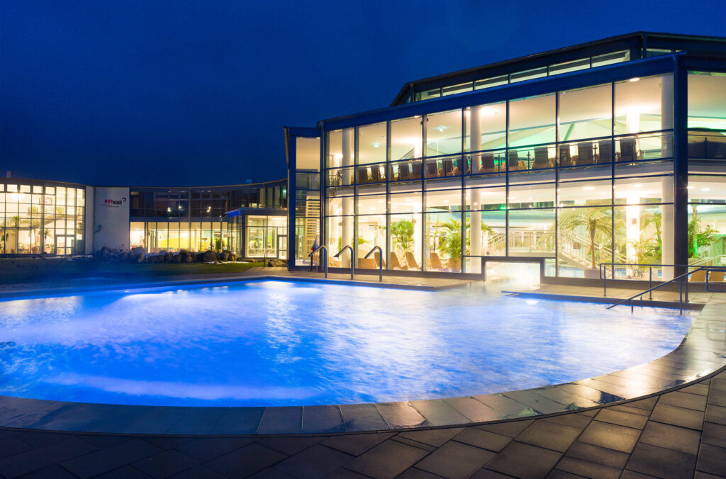 Außenansicht der Siebenquell Therme in Bad Weißenstadt mit beleuchtetem Außenbecken und moderner Glasfassade.